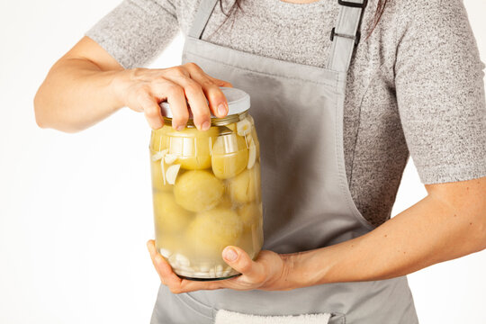 A caucasian woman chef wearing apron is trying to open a stubborn jar lid. She uses force to unscrew the lid in kitchen. Concept image for pickling tomatoes and gherkins and difficulty in opening lids