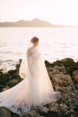 Fototapeta na wymiar Bride in a white dress and veils stands on the rocks by the sea