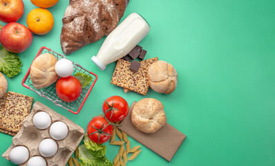 Fototapeta na wymiar Set of fresh products and a miniature shopping basket on a green background top view. Online shopping concept, food delivery. Copy space