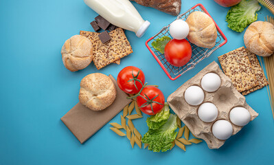 Fototapeta na wymiar Set of fresh products and a miniature shopping basket on a blue background top view. Online shopping concept, food delivery