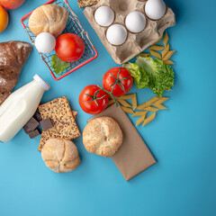 Set of fresh products and a miniature shopping basket on a blue background top view. Online shopping concept, food delivery