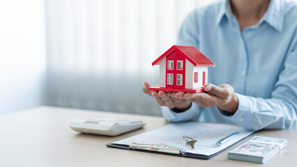 The real estate concept the realtor presenting his work towards his customer by putting the red house model on his palms and raising his hands a little