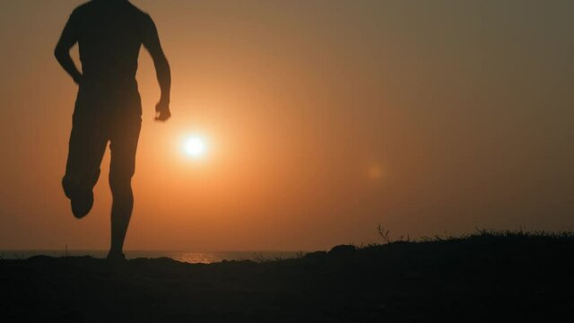 silhouette of active sport athlete male finishing running near sea shore checking run time on beautiful sunset with copy space in California