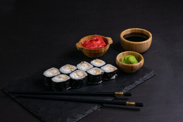 Macro shot of hosomaki sushi with soy sauce on natural black slate plate background with selective focus. Sushi with salmon and avocado