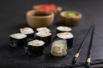Macro shot of hosomaki sushi with soy sauce on natural black slate plate background with selective focus. Sushi with salmon and avocado