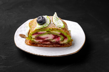 Pistachio roll decorated with blueberries lies on a saucer.