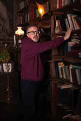 A man on the background of a bookcase with space for text or advertising. Brutal man with glasses 50 years old