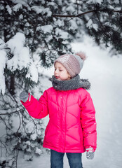 Little girl in a bright jacket plays in the winter forest
