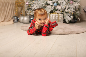 a beautiful little girl in Christmas pajamas red in a cage lies at the Christmas tree