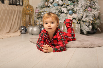 a beautiful little girl in Christmas pajamas red in a cage lies at the Christmas tree