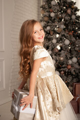 charming little girl 8 years old for the holiday New Year and Christmas 2022 holds a gift of silver color behind her