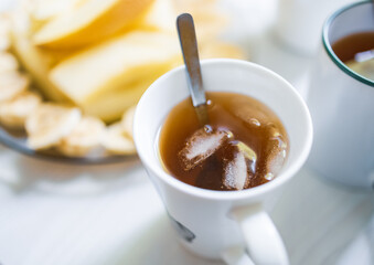 Breakfast with tea and coffee, pieces of fruit, toast with butter and nuts on the table in the kitchen in the morning