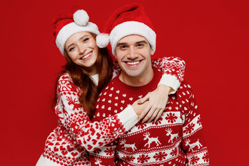 Young fun couple friends two man woman 20s in sweater hat hugging cuddle look camera isolated on plain red background studio portrait. Happy New Year 2022 celebration merry ho x-mas holiday concept.