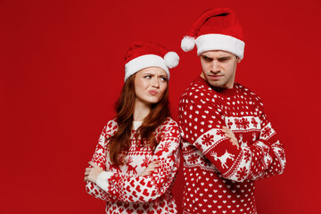 Young sad arguing couple friends two man woman 20s in sweater hat stand back to back isolated on plain red background studio portrait. Happy New Year 2022 celebration merry ho x-mas holiday concept.