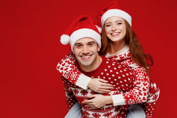 Young fun couple friends two man woman 20s in sweater hat giving piggyback ride to joyful, sit on...