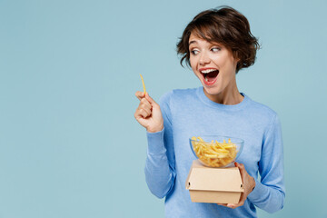 Young smiling cheerful fun cool woman 20s in sweater hold burger french fries potato look aside on...