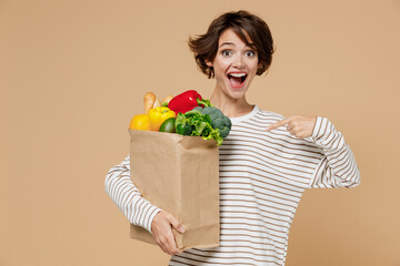 Young smiling amazed excited vegetarian woman in casual clothes hold point finger on paper bag with...