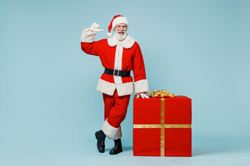 Full body old Santa Claus man in Christmas hat red suit clothes stand near big gift box point on himself isolated on plain blue background studio. Happy New Year 2022 merry ho x-mas holiday concept