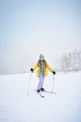 Fototapeta na wymiar Portrait of cheerful skier girl in yellow jacket in a snowy weather