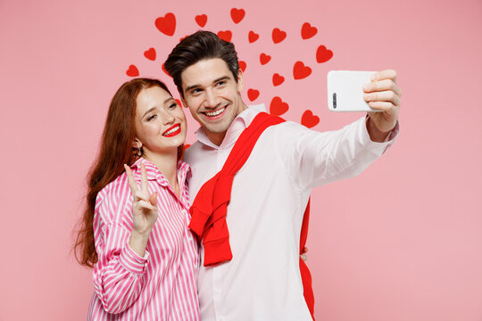 Young couple two friends woman man in casual shirt doing selfie shot on mobile cell phone show v-sign isolated on plain pastel pink background studio. Valentine's Day birthday holiday party concept.