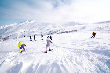 Group of snowboarders freeriding in front of snowy mountains and blue sky