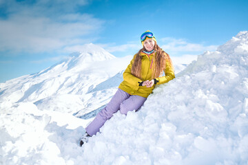 Fototapeta na wymiar Cheerful girl snowboarder in yellow jacket in front of snowy mountains and blue sky