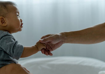 An Asian baby trusts his father's hand to stand up. father and son spending time together