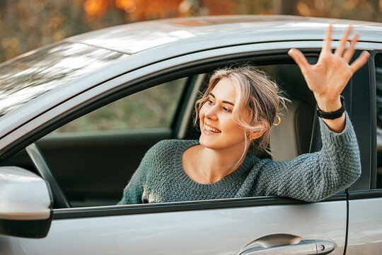 Young Beautiful Women Driving and waving Hand From Open Window, Road trip on autumn, Fun, possitive emotion, waiting for friends