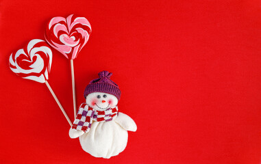 Snowman holding traditional Christmas candies in heart shape on red background. Greeting card concept