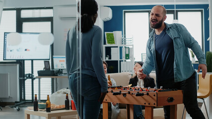 Cheerful man winning soccer game at foosball table, playing football on board with woman after...