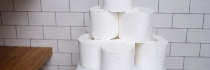 Stack of toilet paper stands on white toilet in bathroom closeup