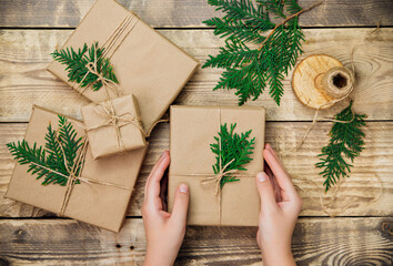 Women's hands pack boxes in kraft paper on a wooden background.Environmentally friendly material.Christmas and New Year.