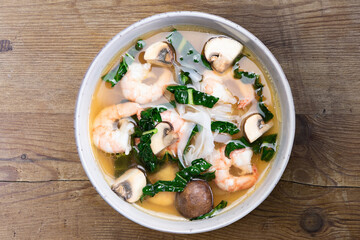 Suppe Brühe Garnelen Shrimps Glasnudeln Gemüse Champignons Pilze Kale Kohl im Teller auf Holzuntergrund