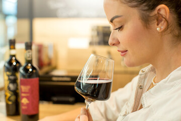 Young attractive woman, tasting wine in a wine store, enjoying glass of tasty wine
