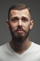 Obraz premium Men's emotions concept. Emotive portrait of upset charismatic young bearded man posing over light gray background. Perfect haircut. Hipster style. Close up. Studio shot