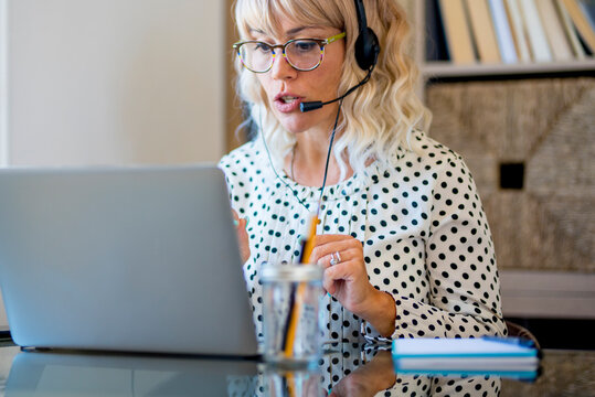 Busy adult woman at work at laptop computer calling on headphones and microphones. Concept of modern online job female people. Attractive lady with eyewear in communication