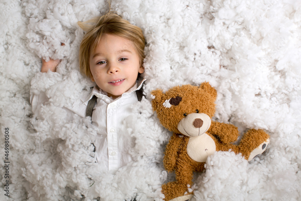 Poster Cute fashion toddler boy, playing in the snow with teddy bear in front of a wooden cabin log