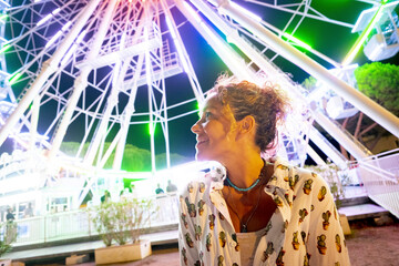 Portrait of happy adult woman with panoramic wheel in background. People enjoy night life and...