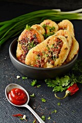 Homemade savory pancakes (Fritters) with minced meat pieces, dill, parsley and green onions, garlic, tomato sauce and chili peppers on a dark background. 