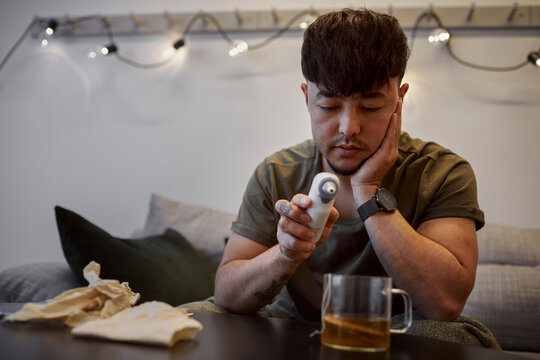 Ill man on sofa checking thermometer