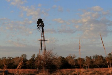 A shot of a colorful Kansas Sunset with a farm Windmill silhouette with tree's and clouds north of Hutchinson Kansas USA out in the country in a farm pasture.