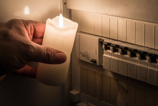 Sicherungskasten mit Sicherungen in einem Verteilerkasten während eines Stromausfall mit weißer Kerze beleuchtet die ein Mann in der Hand hält, Deutschland