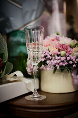 On the table are bouquets of flowers and glasses of champagne on the background of gifts.