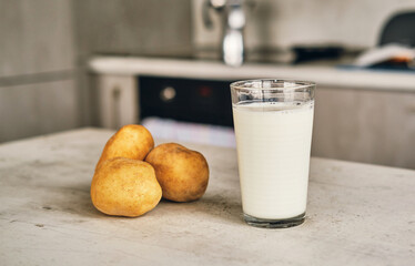 A transparent glass with potato milk on the table next to the potato tubers. 