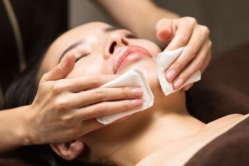 コットンで女性の顔を拭いている。