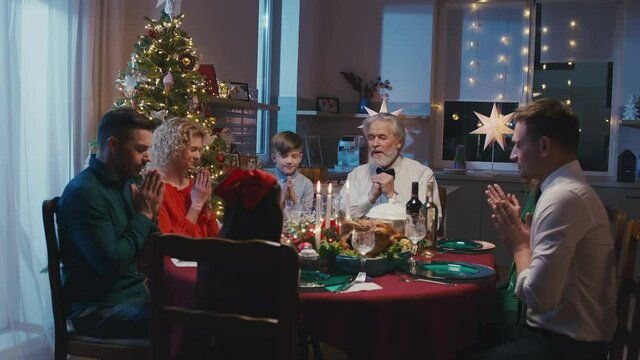 Loving family started praying before Christmas dinner at home. Beautiful friends sitting at dining table set with delicious food during New Year party.