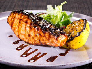 grilled salmon fillet poured with teriyaki sauce on a plate with salad mix and grilled slice of lemon