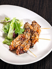 portion of grilled chicken wings skewers with mix salad on a plate on dark background