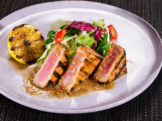 grilled tuna fillet served with salad mix and grilled lemon on a plate on dark background