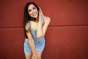 Fototapeta premium Young happy woman listening to music outdoors. Positive hipster girl with headphones enjoying in sunny day..